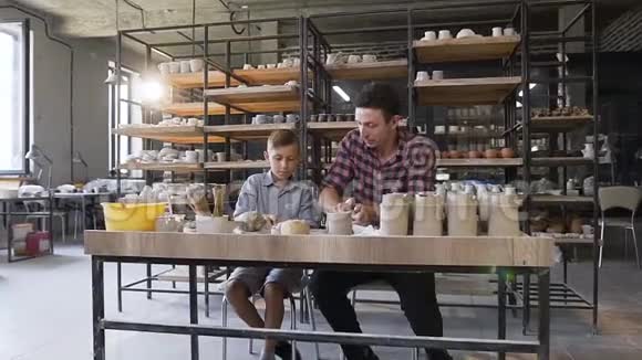 可爱的白种人男孩和他的父亲揉捏陶罐的粘土视频的预览图