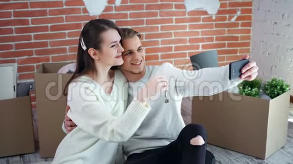 幸福的年轻夫妇带着钥匙在新公寓里自拍用智能手机中镜头拍摄视频的预览图