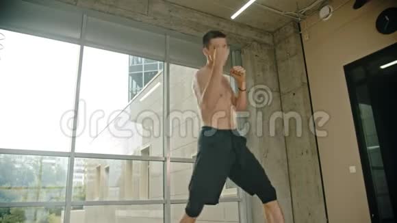 一个运动的赤膊男子拳击手站在窗边用一种影子耐力训练来进行一场战斗视频的预览图