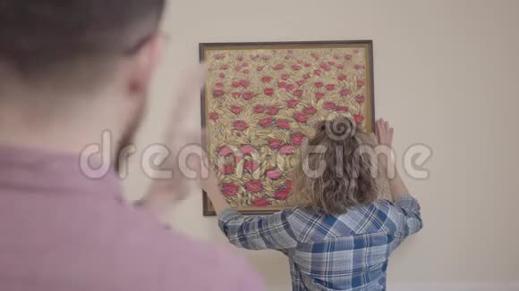 年轻的家庭搬到了一套新公寓搬到新家的概念妻子挂着一张照片丈夫很高兴视频的预览图