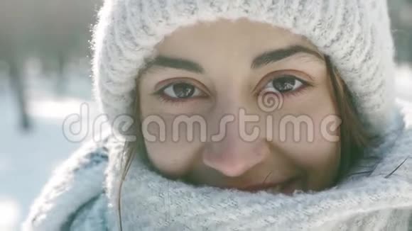 美丽的笑着的年轻女子穿着温暖的羊毛帽戴着长长的围巾在白雪皑皑的冬天公园里在毛茸茸的地方做着特写肖像视频的预览图