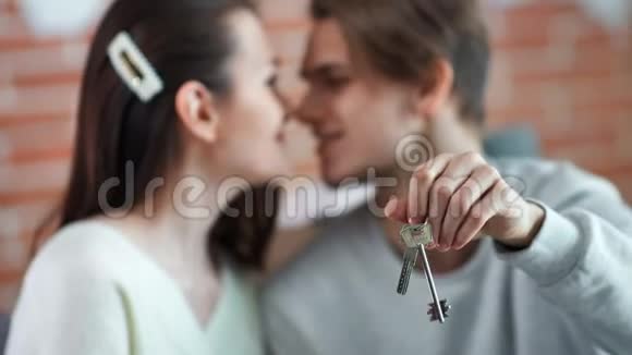 特写男性手拿着新公寓的钥匙一对夫妇在背景中感受爱情视频的预览图