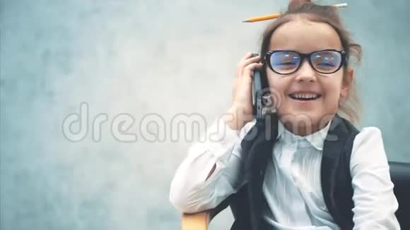 一个小商业女孩坐在灰色背景的椅子上的特写在这期间他通过电话和微笑说话视频的预览图