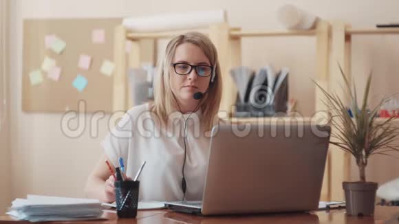 穿着白色上衣和眼镜的女孩白种人的外表为办公室里的笔记本电脑工作并向人们提供建议视频的预览图