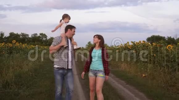 一家人带着小宝宝走在路上在向日葵的田野旁边笑小孩骑着他父亲视频的预览图