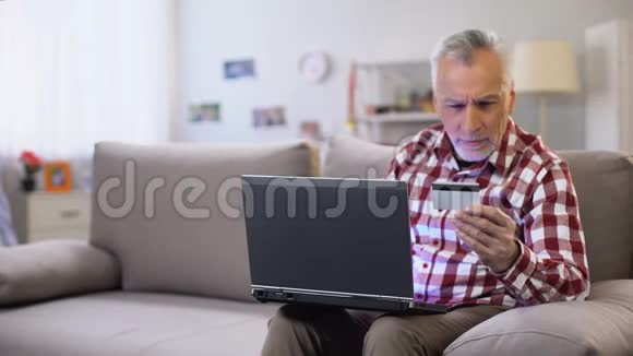 退休男性在笔记本电脑上插入信用卡号码在线支付申请视频的预览图