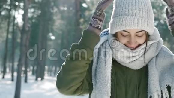 在白雪皑皑的冬季公园里穿着温暖的羊毛帽和长围巾的美丽欢笑的年轻女子的慢镜头特写肖像视频的预览图
