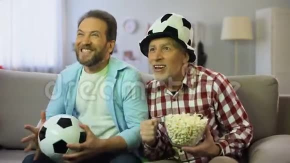 爸爸和儿子兴奋地为最喜欢的足球队欢呼在电视上看比赛视频的预览图