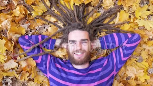 微笑的人躺在秋天公园的落叶上视频的预览图