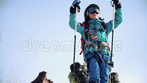 一位年轻的女孩登山者在山顶上欢欣鼓舞她高兴地笑着挥动她的滑雪杆视频的预览图