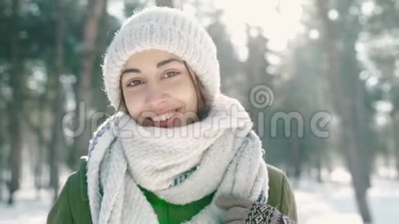 美丽的笑着的年轻女子戴着温暖的羊毛帽戴着长长的围巾在白雪皑皑的冬天公园里在毛茸茸的地方慢镜头肖像视频的预览图