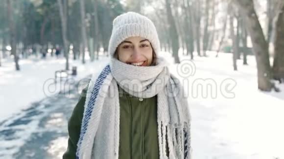 慢镜头描绘美丽快乐微笑的年轻女子穿着温暖的冬衣在白雪皑皑的冬公园散步视频的预览图