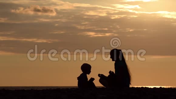 妈妈和儿子在海滩上玩耍学习香蕉日落时间剪影视频的预览图