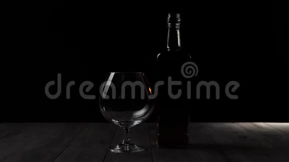 豪华白兰地一个方形瓶子里的金色干邑站在黑色背景的木桌上的玻璃旁边视频的预览图
