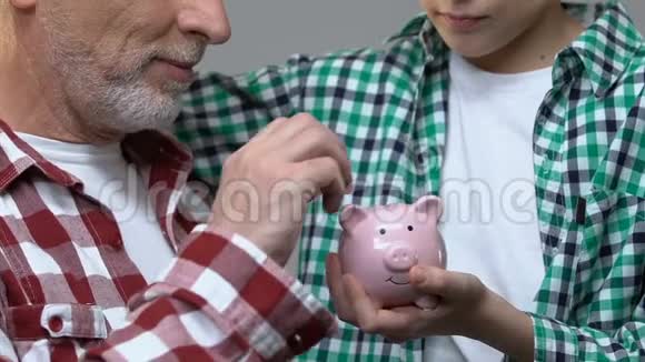 男孩拥抱祖父老人把硬币放在储蓄罐里储蓄观念视频的预览图