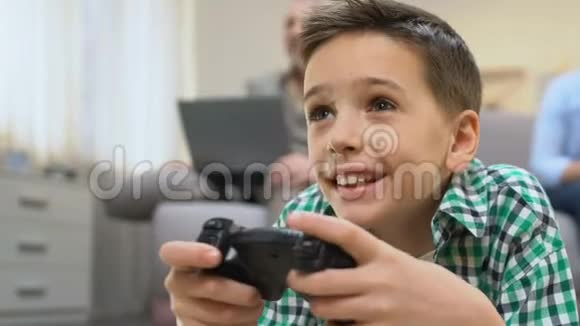 男孩玩电子游戏爷爷在后台使用笔记本电脑缺乏沟通视频的预览图