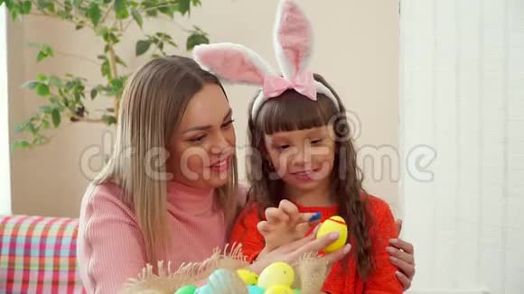 妈妈转动鸡黄蛋女儿用手指在蓝点上画戴着兔耳朵的女式头巾视频的预览图