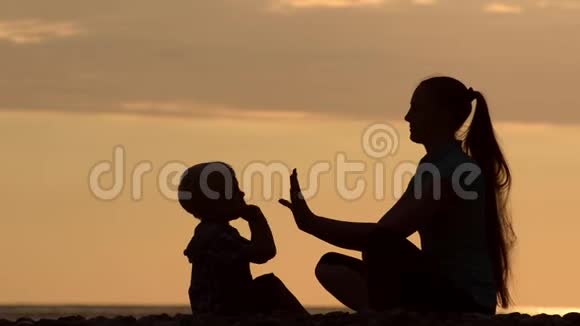 妈妈和儿子在海滩上玩双手游戏日落时间剪影视频的预览图