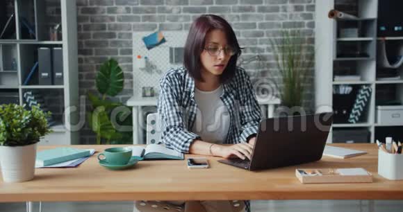年轻女子在办公室打手提电脑然后在笔记本上写字视频的预览图