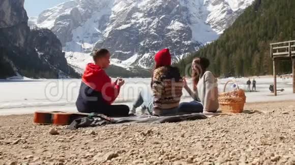 年轻人旅行坐在海岸上吃面包背景上美丽的山视频的预览图