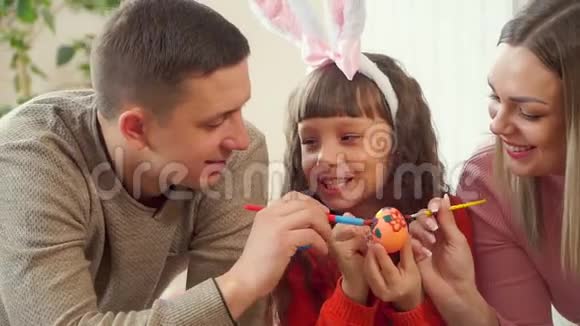 爸爸妈妈帮女儿用画笔装饰复活节彩蛋幸福的家庭一起准备复活节视频的预览图