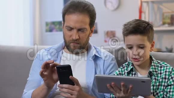 男孩使用平板电脑父亲在家里在智能手机上滚动缺乏沟通视频的预览图
