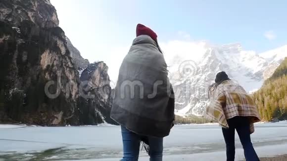 两个年轻的旅行妇女被覆盖在毯子里走在冰冻的湖面上视频的预览图