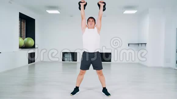 人用水壶铃做蹲式动作工作室里的一个人举起重物做一个蹲视频的预览图