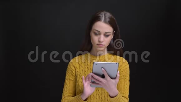 一幅长头发的黑发女孩穿着黄色毛衣专心地用平板电脑和摄像机观看的肖像视频的预览图