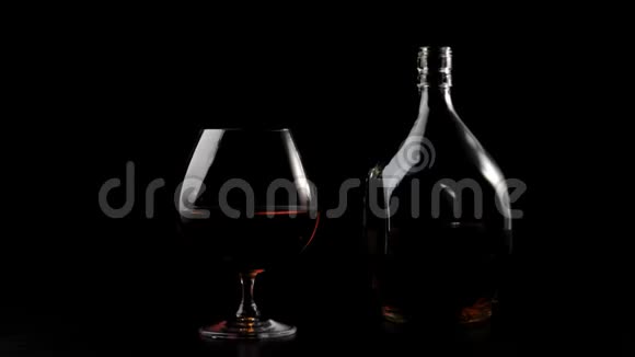 豪华白兰地一个方形瓶子里的金色干邑站在黑色桌子上的玻璃旁边背景是黑色的玻璃眩光视频的预览图