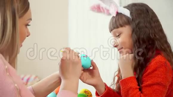 女儿拿着一个蓝色的鸡蛋妈妈用红色的画笔在上面画了一个波浪状的图案视频的预览图