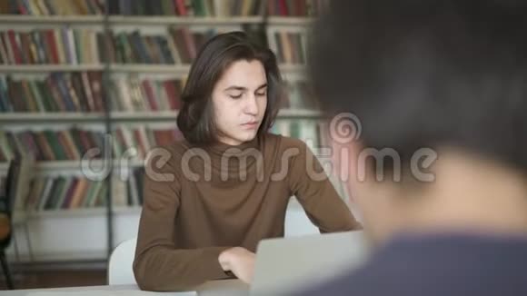 中镜头的男生坐在图书馆里茫然地看着笔记本电脑视频的预览图