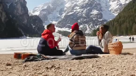 年轻人旅行坐在海岸上吃面包背景上美丽的山视频的预览图