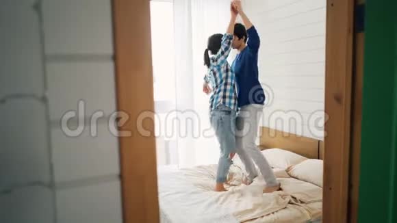 快乐的年轻恋人们在家里的床上跳舞在卧室里玩得很开心漫不经心地笑着快乐的青春现代视频的预览图