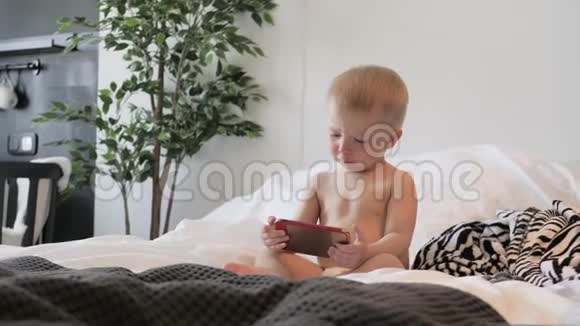 小男孩在家里的床上看智能手机上的卡通生活方式视频的预览图