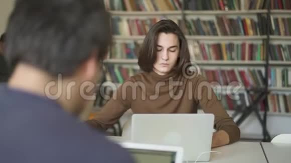 中镜头的学生男性坐在图书馆里茫然地看着笔记本电脑视频的预览图