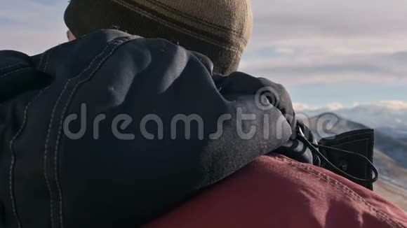 一个穿着温暖夹克和帽子的白人男子在冬天在山上近距离观看Elbrus视频的预览图
