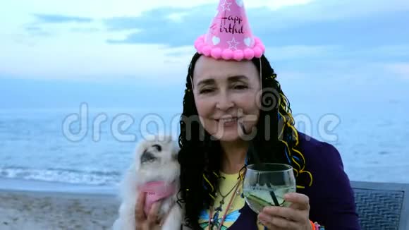 快乐成熟的成年女性白种人戴着生日帽和她的狗一只白色的北京人视频的预览图