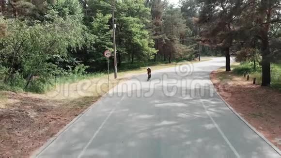 漂亮自信的年轻骑自行车女孩穿着运动服骑着车穿过夏天的公园空中无人机视野视频的预览图