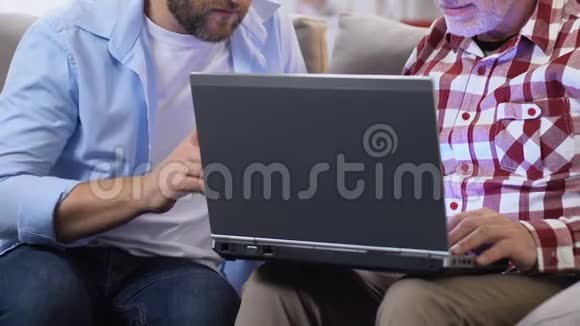 儿子向成年父亲展示如何在笔记本电脑上打视频电话现代技术视频的预览图