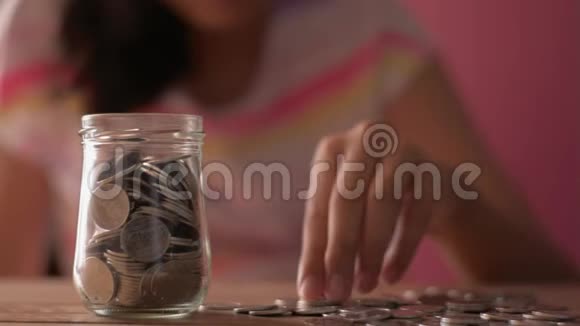 穿着休闲装的小女孩把钱放进玻璃罐里以备将来之需视频的预览图