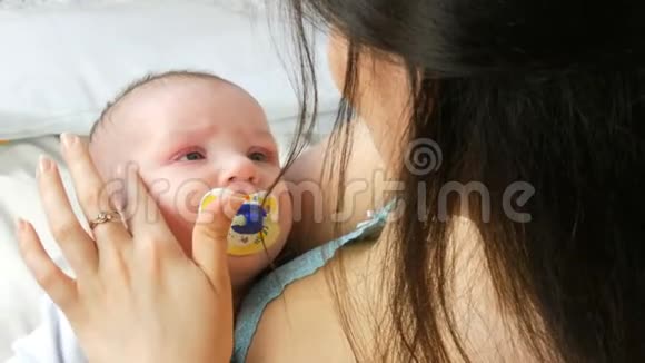 一位美丽的年轻长发母亲轻轻地抚摸着她新生的婴儿抱在怀里坐在床上这就是视频的预览图