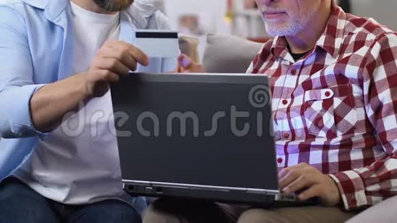 儿子向父亲出示信用卡并解释如何使用笔记本电脑视频的预览图