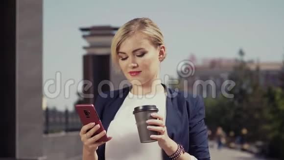 白人女孩穿着西装走在街上喝着咖啡看着他的手机视频的预览图