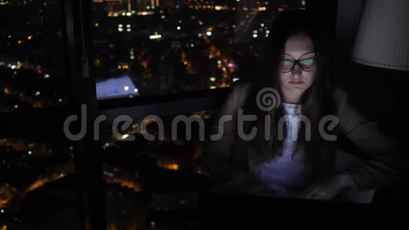 年轻的女性自由职业者晚上在家窗户附近工作视频的预览图