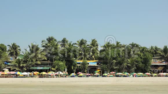 人们和海滩上的人在阳光明媚的五颜六色的雨伞下在沙滩上背景是绿色的酒吧和餐馆视频的预览图