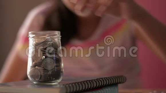 穿着休闲装的小女孩把钱放进一个玻璃罐子里接受教育视频的预览图