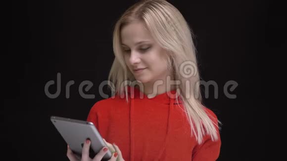 年轻的白发白种人穿着红色毛衣微笑着在黑色上显示绿色的平板电脑屏幕和手指标志视频的预览图