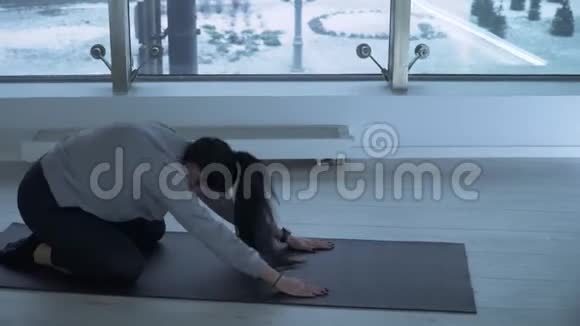 年轻女子在健身房的垫子上做瑜伽有大的落地窗运动女士伸展手臂和弯曲视频的预览图