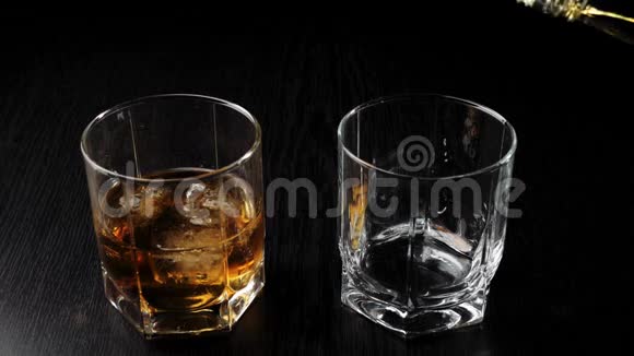 豪华威士忌手把金色的威士忌从一个方形的瓶子里倒入一个玻璃杯放在靠近玻璃杯的黑桌上里面有威士忌和冰视频的预览图